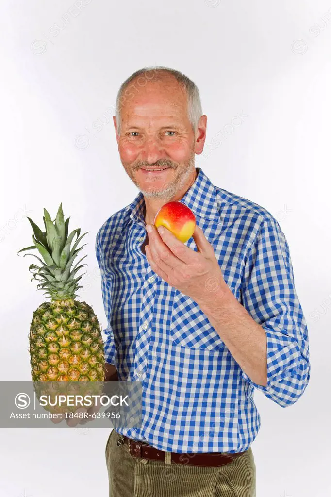 Elderly man holding a pineapple and and apple in his hands