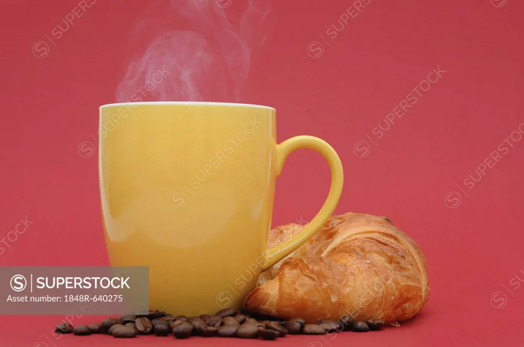 Steaming coffee cup with coffee beans and a croissant
