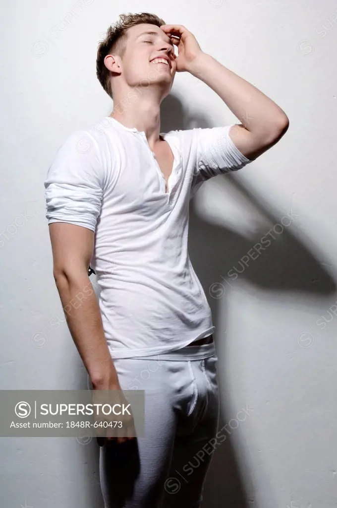 Young man wearing white underwear, leaning against wall