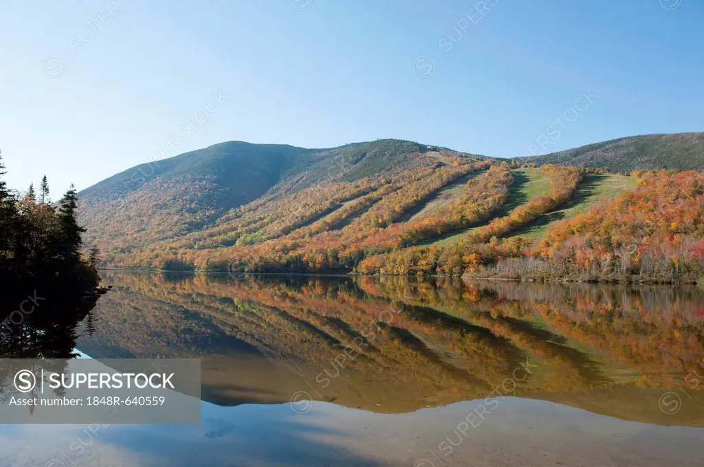 Ski slopes in autumn reflected in Profile Lake, foliage coloured during Indian Summer, Franconia Notch State Park, White Mountains National Forest, Ne...