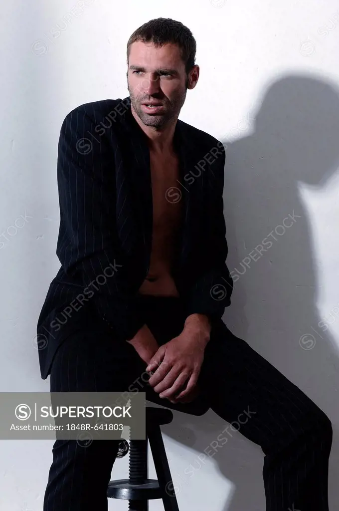 Man, 37 years, wearing a suit without a shirt, sitting on stool