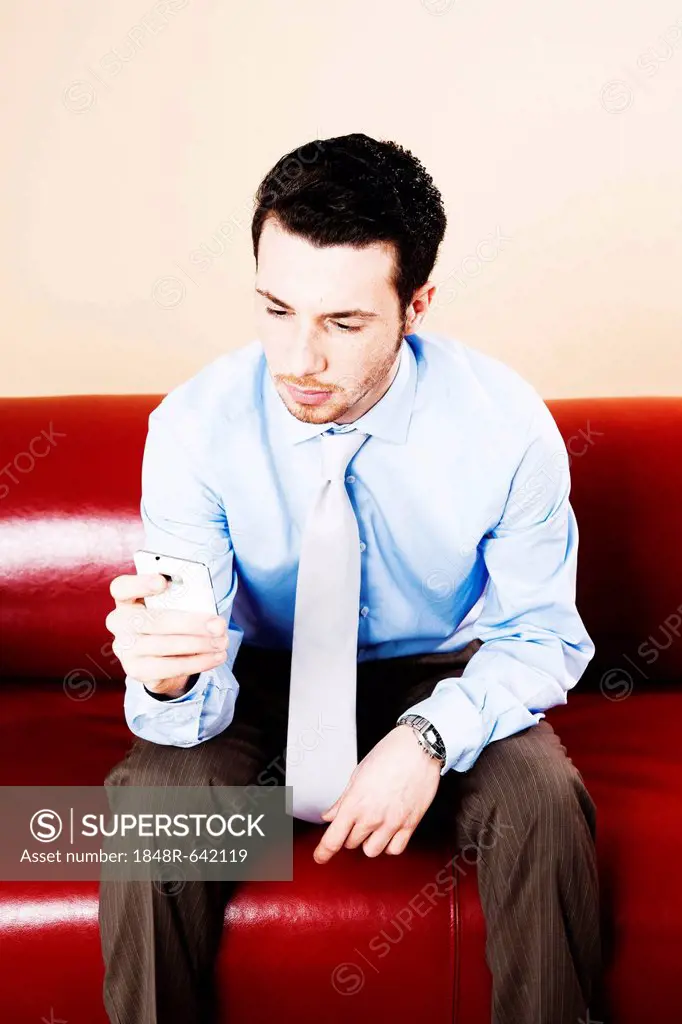 Young manager sitting with a smartphone on a sofa