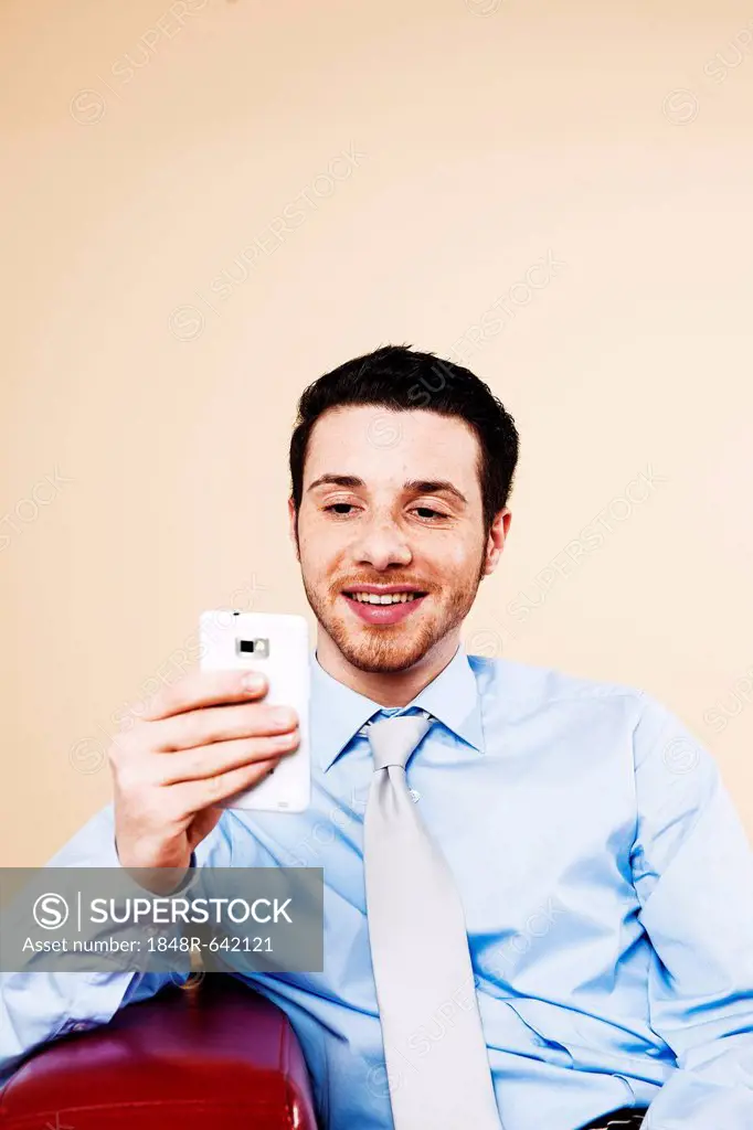 Young manager sitting on a sofa with his smartphone and checking an SMS