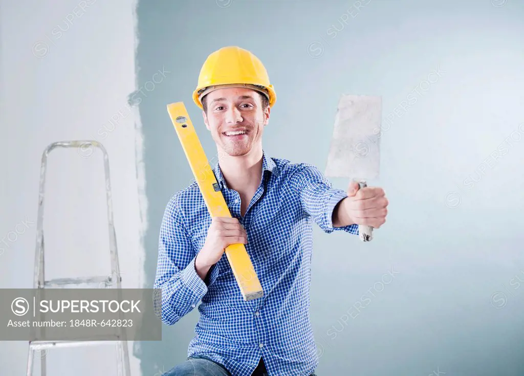 Young tradesman holding a spirit level and a trowel