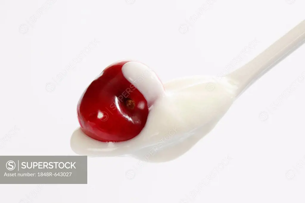 White plastic spoon with yogurt and a cherry