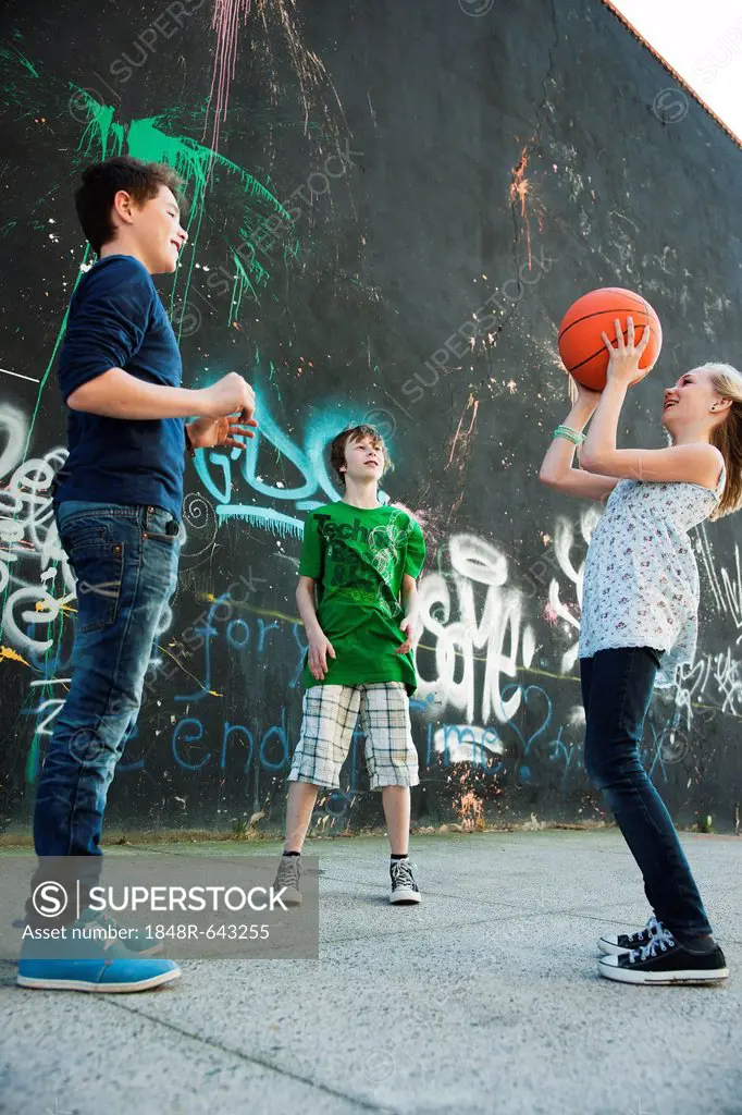 Three friends playing basketball in front of a graffiti wall
