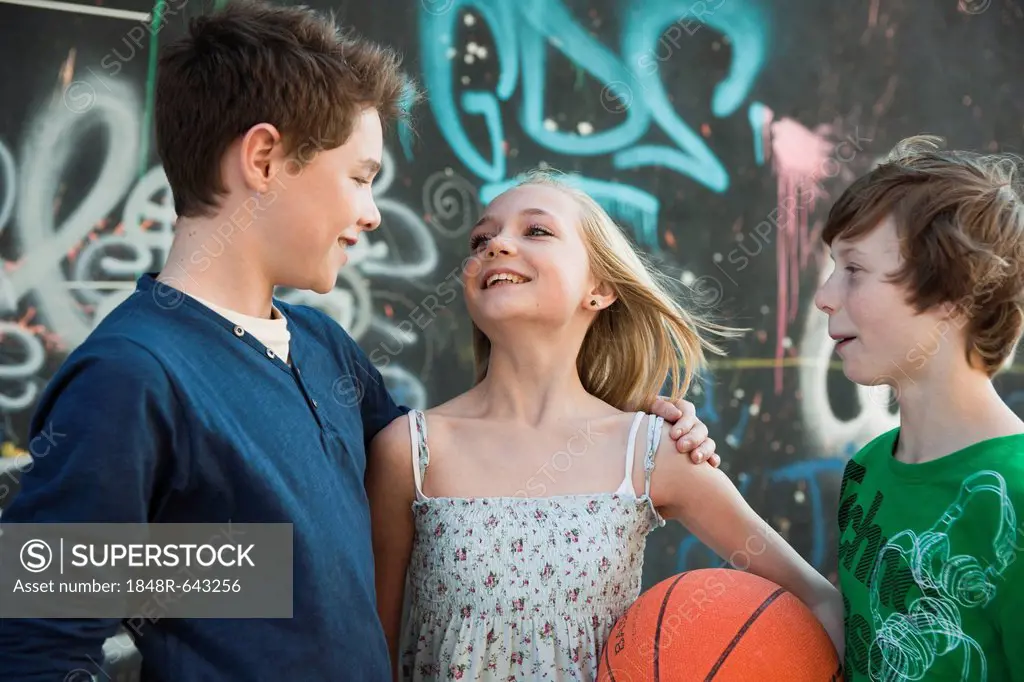 A girl holding a basketball asking two boys to play with her