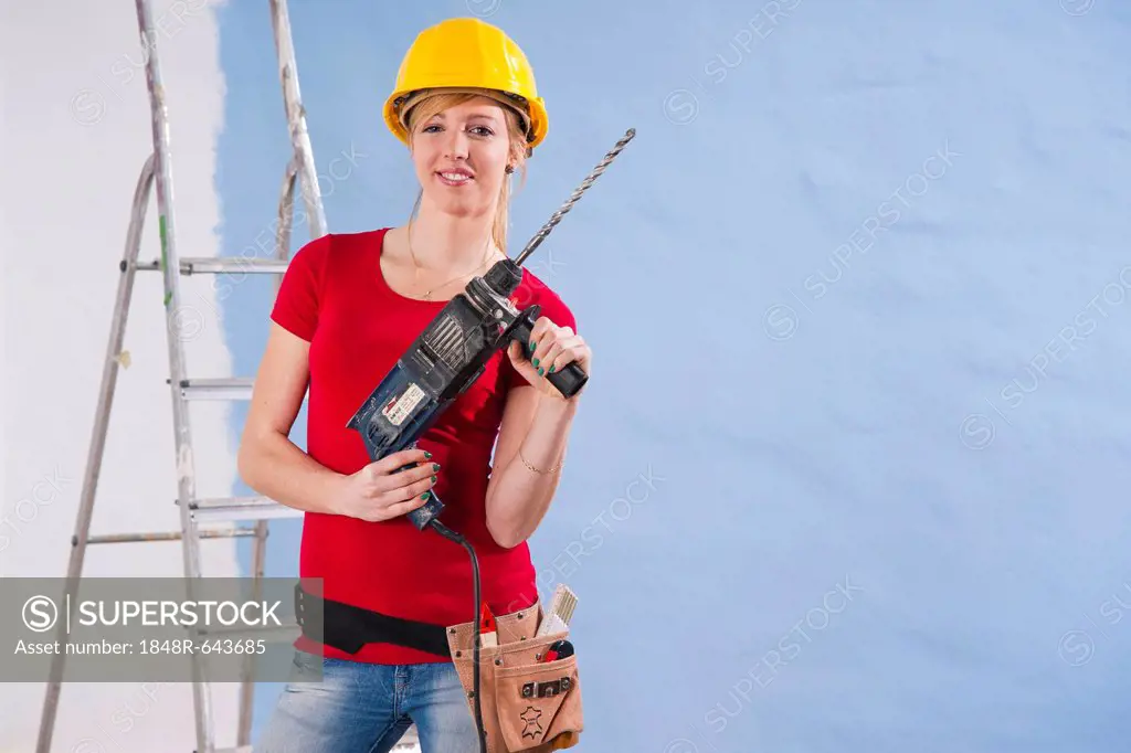 Young woman wearing a yellow safety helmet and holding a drill