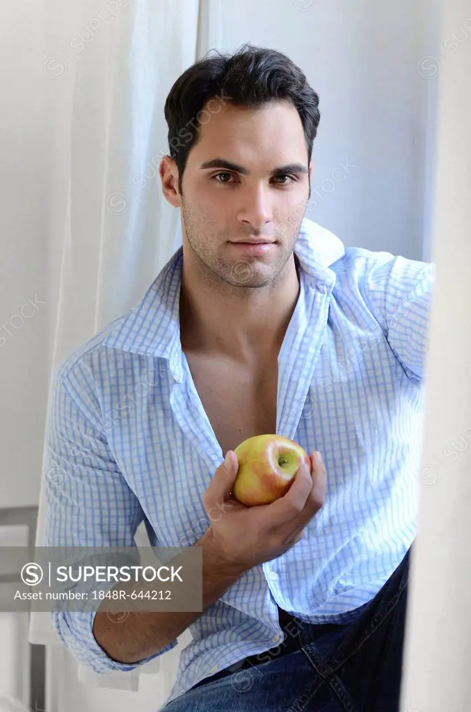 Young man sitting on a window sill eating an apple