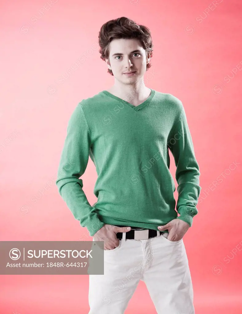 Young man wearing a green sweater standing casually in front of a red wall
