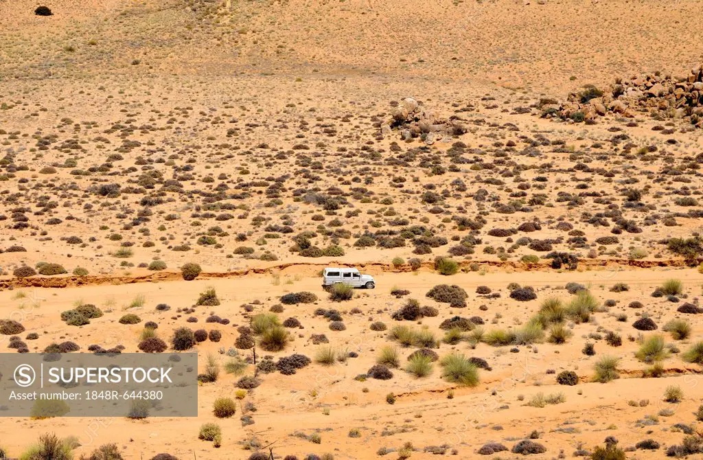 Four-wheel-drive vehicle crossing the rugged, sparsely covered with low bushes, semi-desert landscape of Goegap Nature Reserve, Namaqualand, South Afr...