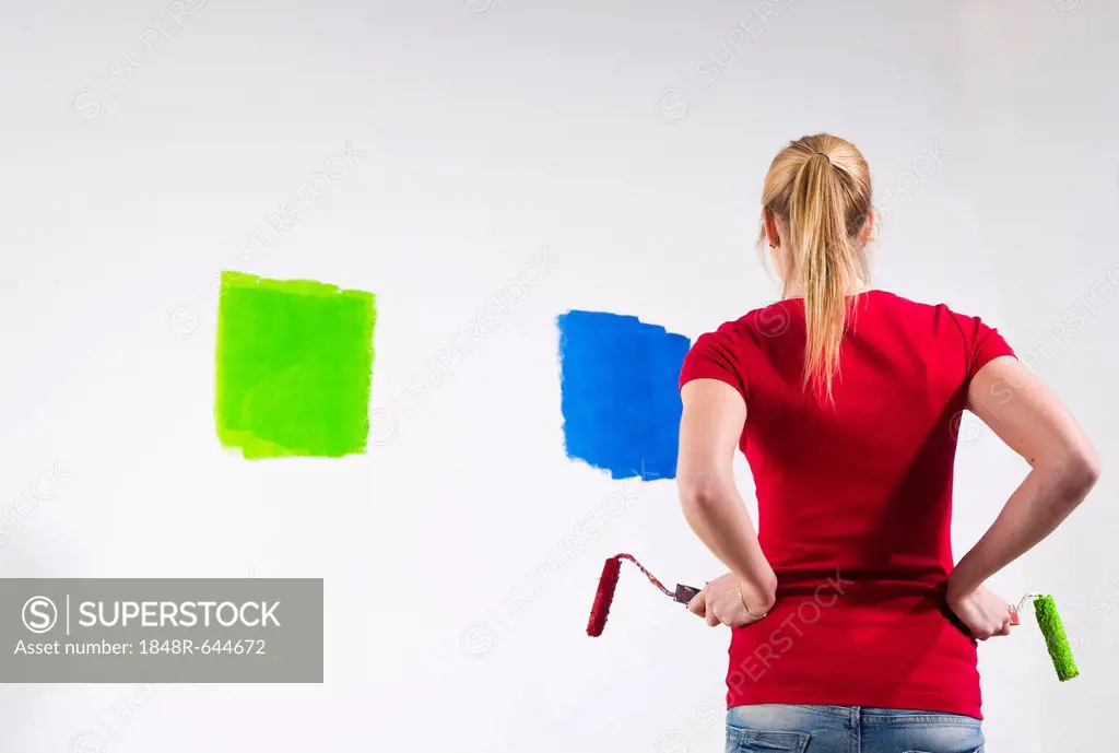 Young woman holding two paint rollers in front of a wall with paint samples