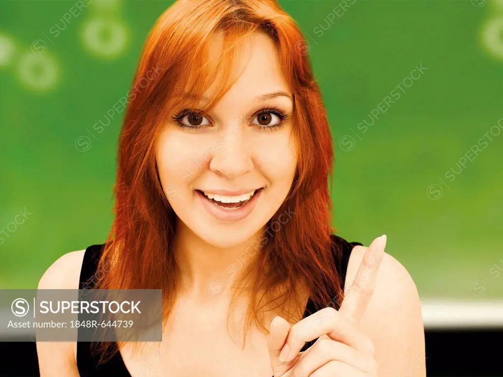 Young smiling teacher with a wagging finger, in front of a school board