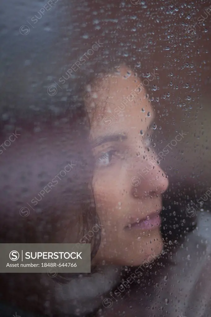 Pensive woman behind a window with rain drops