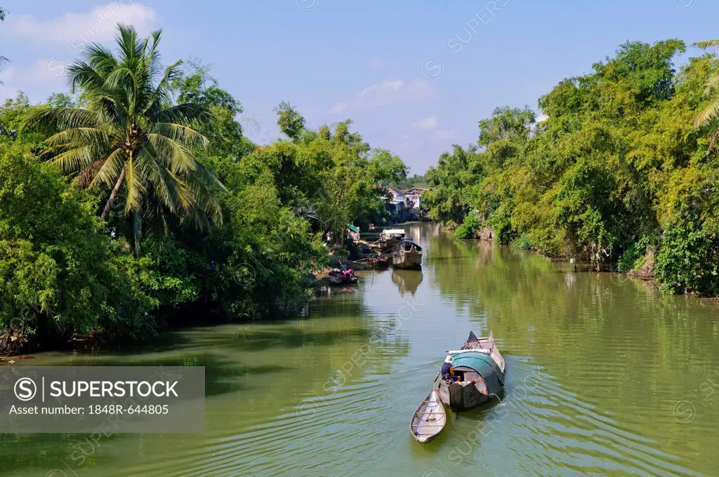 Small wooden motorboat passing through a water channel surrounded by tropical vegetation, Hue, Vietnam, Asia