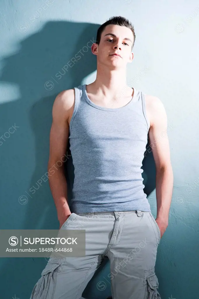 Cool young man wearing a singlet, leaning against a wall