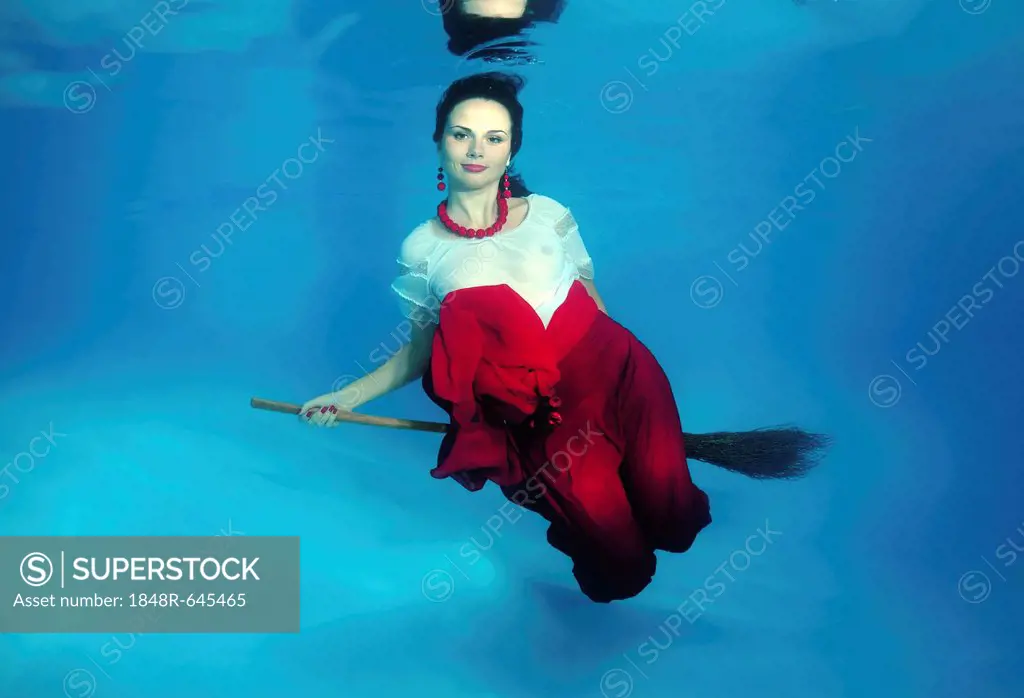 Witch on a broomstick, woman presenting underwater fashion in pool