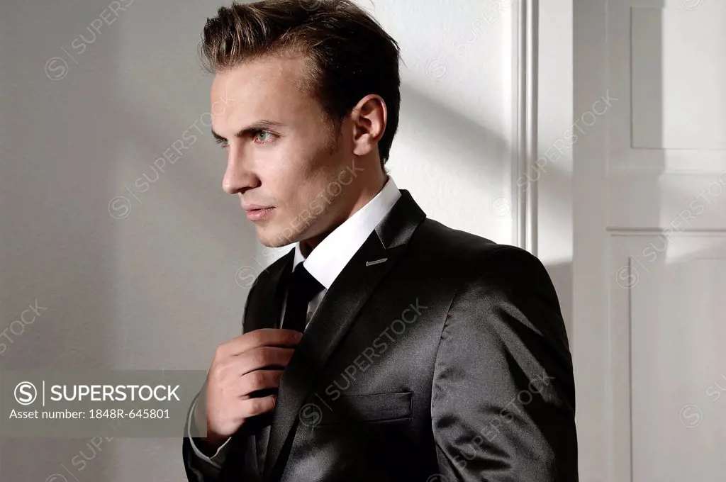 Fashion image, young man wearing a suit, straightening his tie