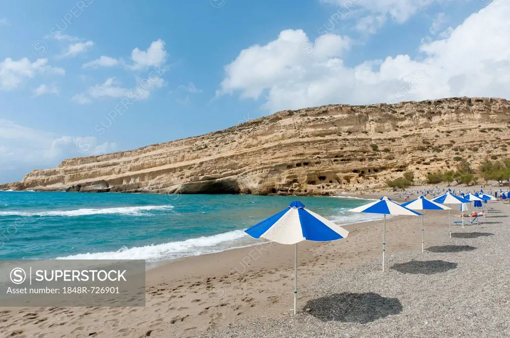Neolithic cave dwellings in the yellow sandstone, parasols on the beach of Matala, former site of the hippies, Crete, Libyan Sea, Mediterranean, Greec...