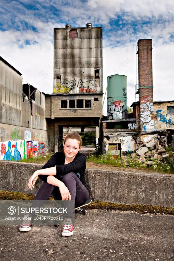 Portrait of a young teenage girl sitting on a skateboard in an urban area