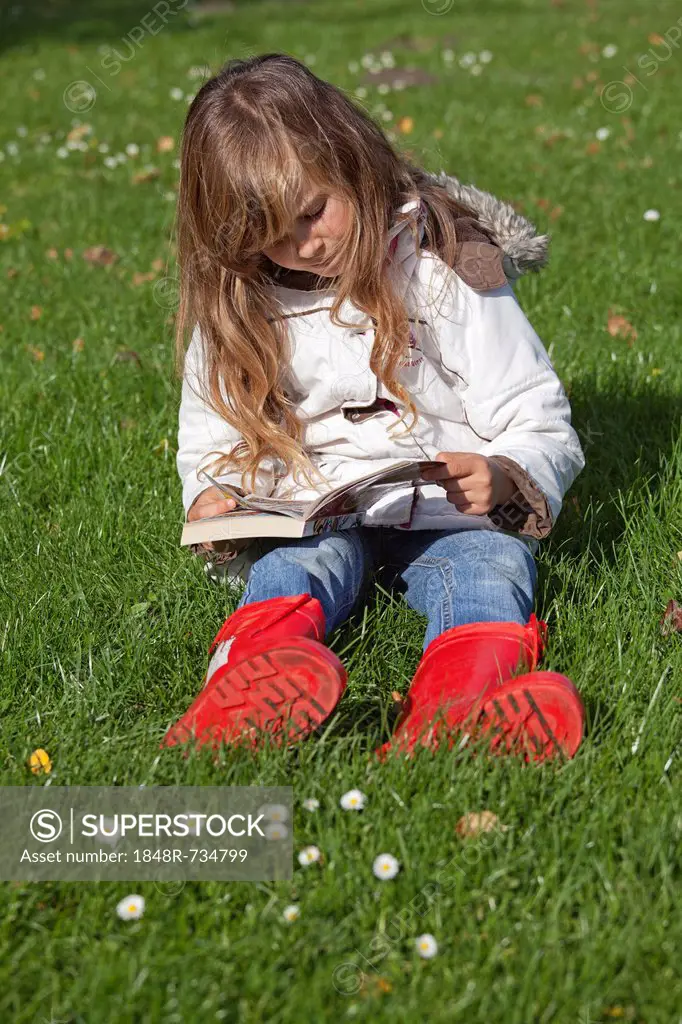 Little girl sitting on the grass and reading a comic