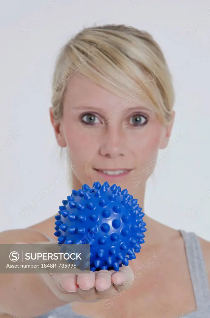Young woman with her arm outstretched and holding a blue spiky massage ball in her hand