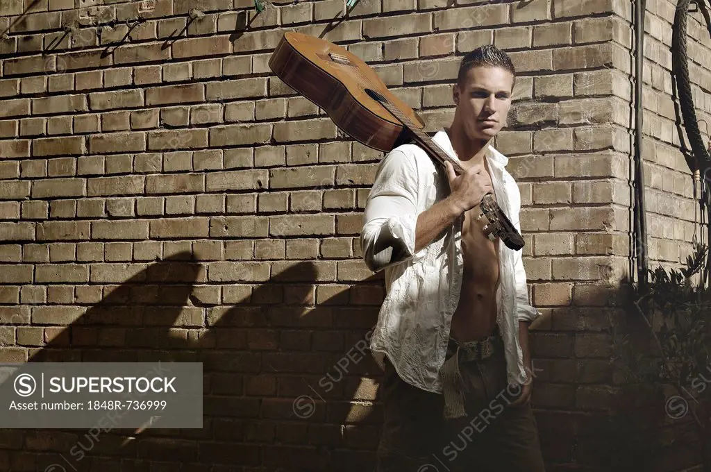 Young man holding a guitar in front of a wall