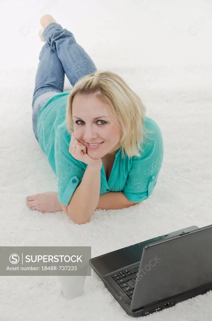 Woman lying on carpet with laptop and mug in front of her
