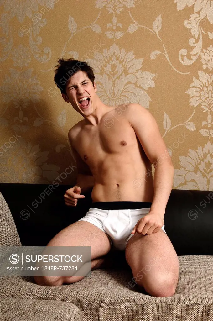 Young man wearing underwear kneeling on a sofa