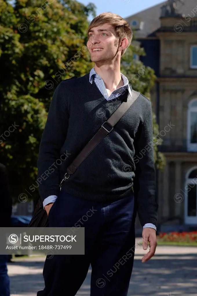 Young man wearing elegant clothing with a bag over his shoulder in front of the New Palace in Stuttgart, Baden-Wuerttemberg, Germany, Europe