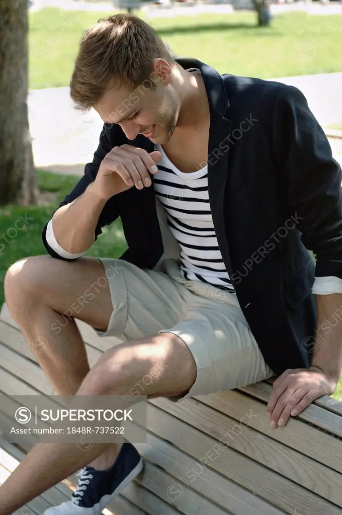 Young man in casual outfit sitting on a park bench in a park,