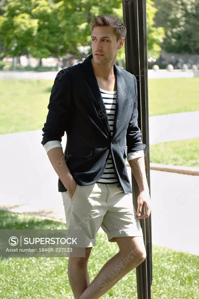 Young man in casual outfit leaning on a lamppost in a summerly park