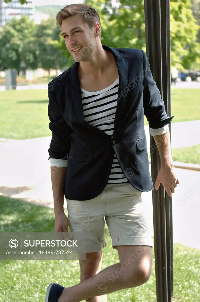 Young man in casual outfit leaning on a lamppost in a summerly park