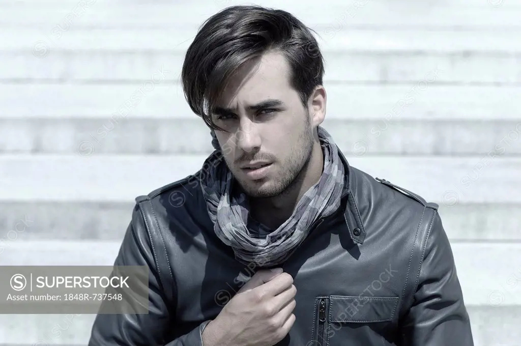 Young man wearing a leather jacket in front of an open staircase, portrait of a young rocker