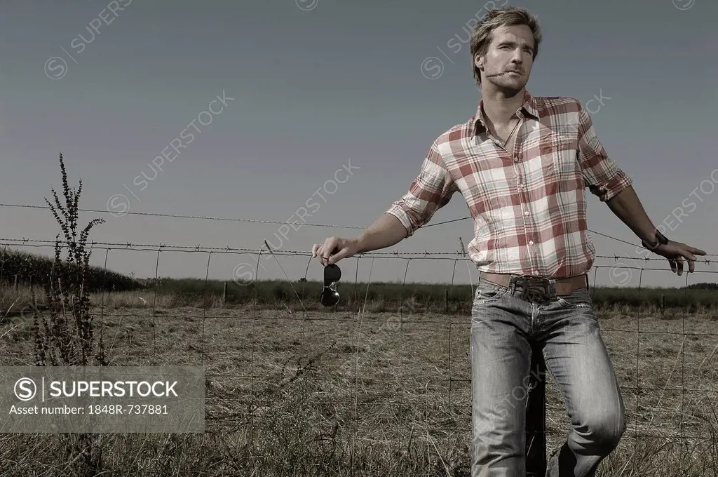 Cowboy leaning against a wire fence