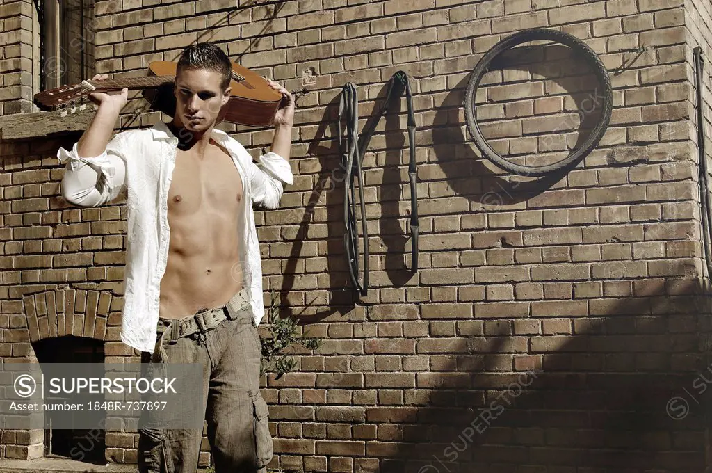 Young man holding a guitar in front of a wall