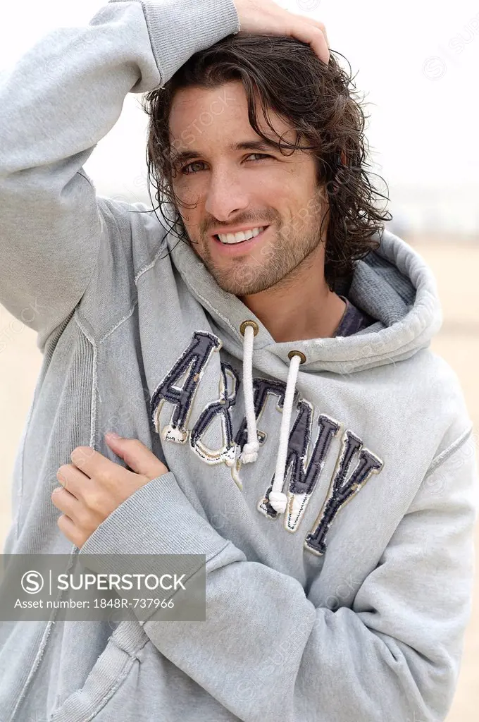 Man, early 30s, wearing a hooded sweater in bad weather at the beach