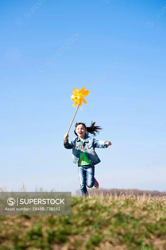 Girl running happily while holding up a pinwheel in a field