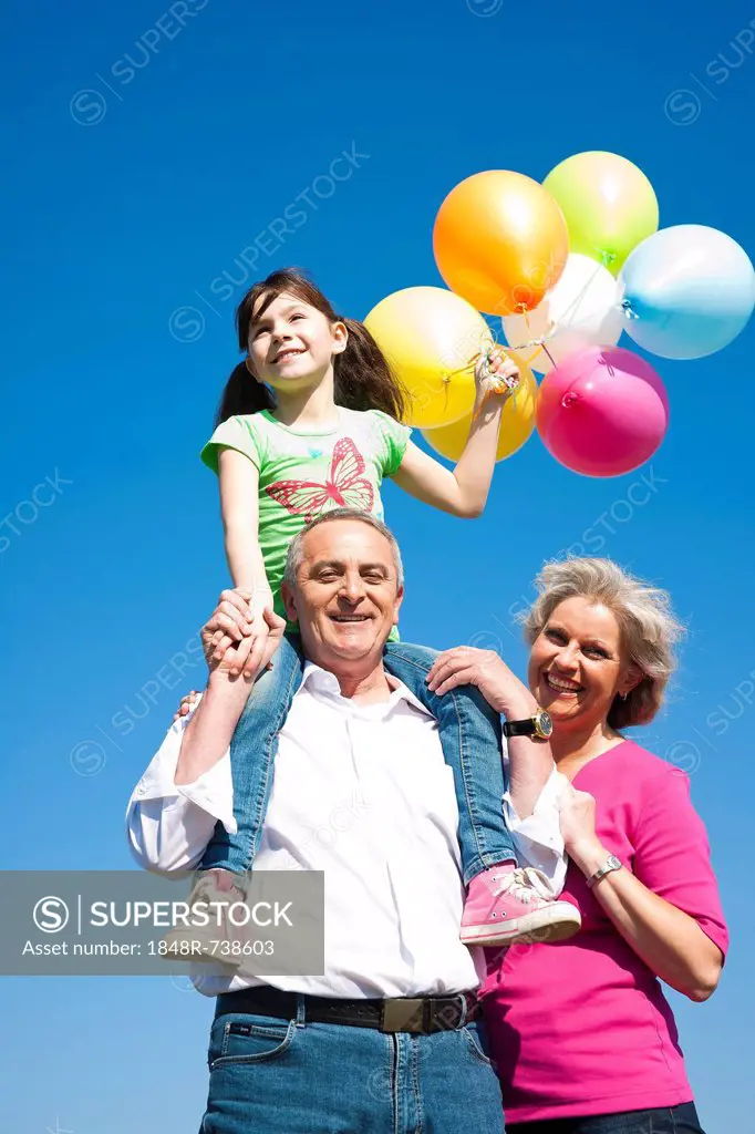 Grandparents holding their granddaughter while she is holding coloured balloons in her hand