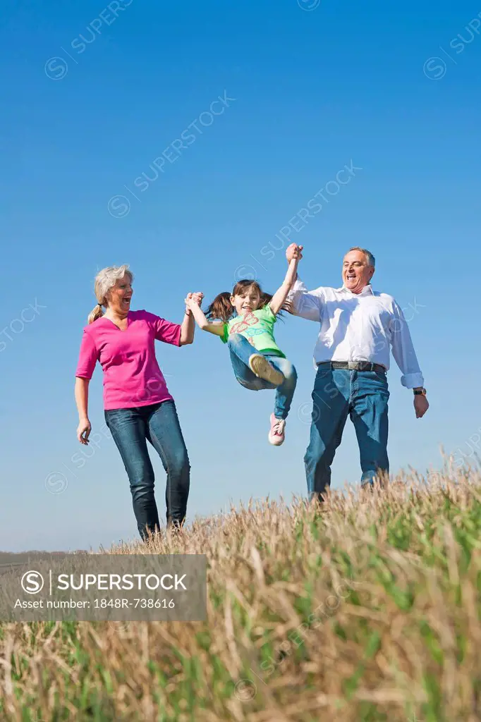 Grandparents swinging their granddaughter in the air with their hands