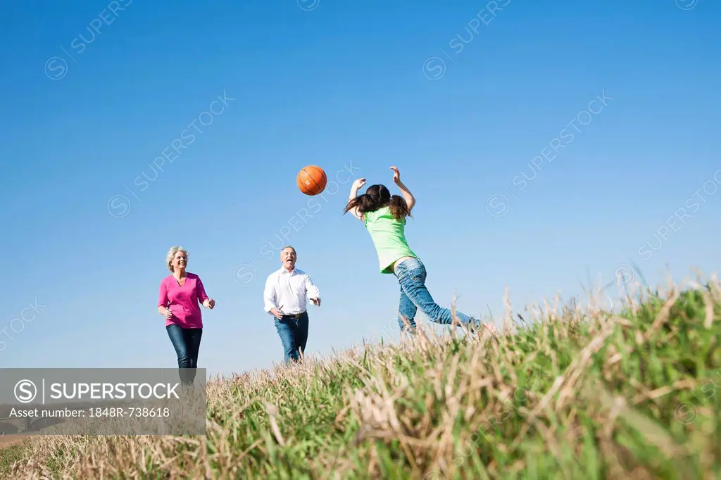 Girl playing ball with her grandparents on a meadow