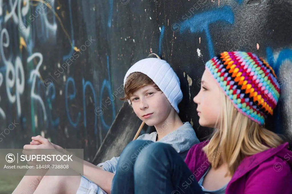 Boy and girl sitting in front of a wall with graffiti
