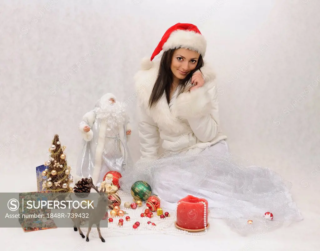 Young woman with Santa hat and a white faux fur jacket surrounded by Christmas decorations