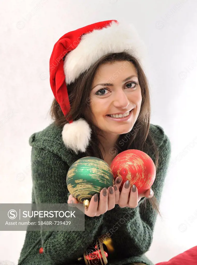 Young woman with Santa hat holding two Christmas baubles