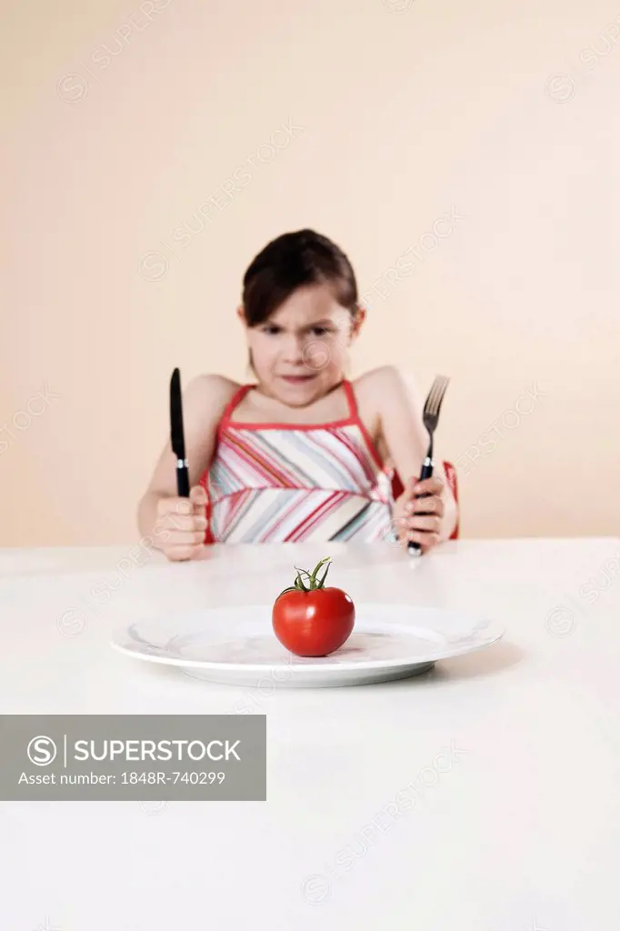 Girl holding a knife and a fork looking disgustedly at a tomato