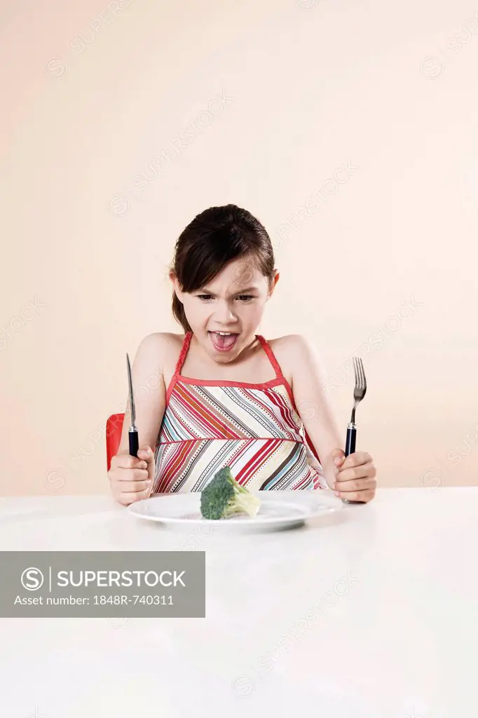 Girl holding a knife and a fork looking disgustedly at a piece of broccoli