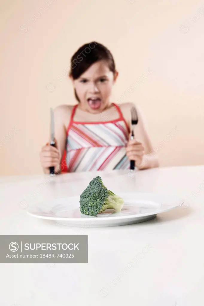 Girl holding a knife and a fork looking disgustedly at a piece of broccoli
