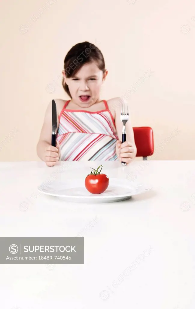 Girl holding a knife and a fork looking disgustedly at a tomato