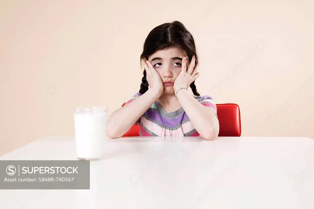 Girl looking listlessly at a glass of milk