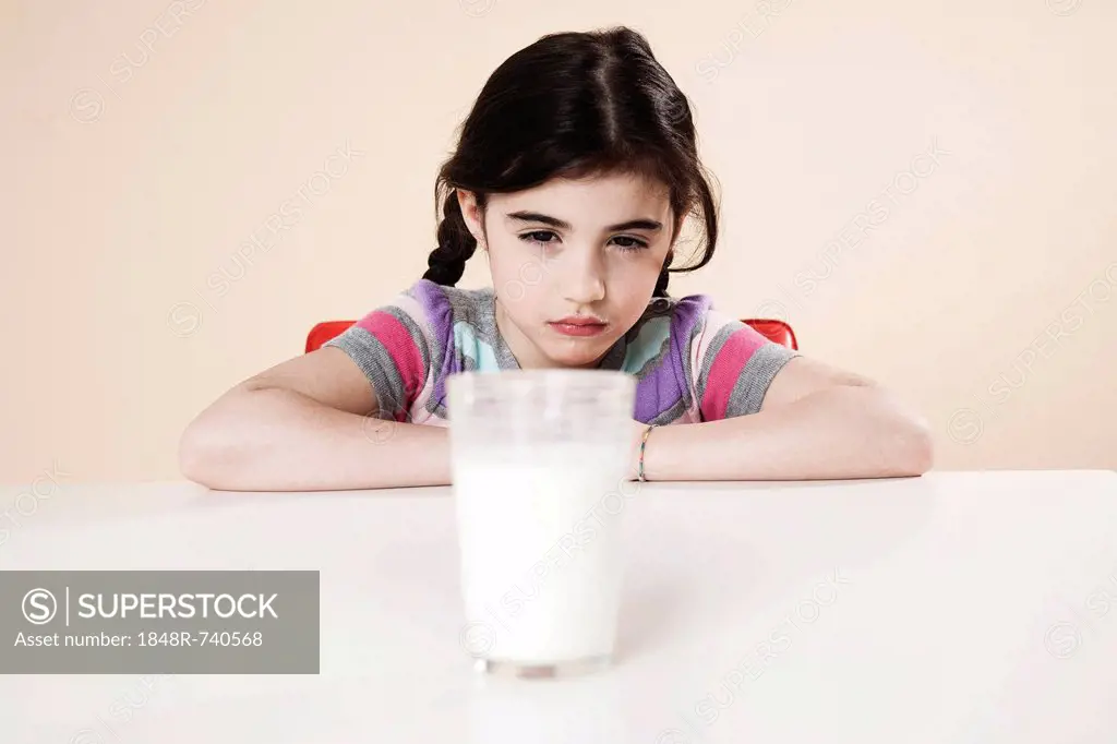 Girl looking listlessly at a glass of milk